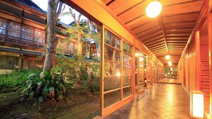 A corridor with wooden walls and glass doors, leading to a traditional building with a tiled roof. - Arai Ryokan (Izu)