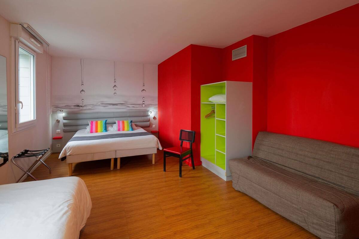 A bedroom with a bed, a chair, a sofa, a wardrobe, and a window.