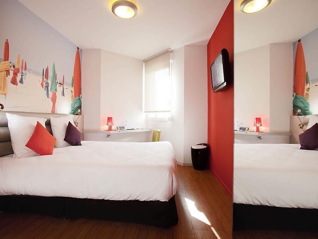 Habitació d'hotel amb dos llits, un finestral gran, televisió penjada a la paret i un quadre.