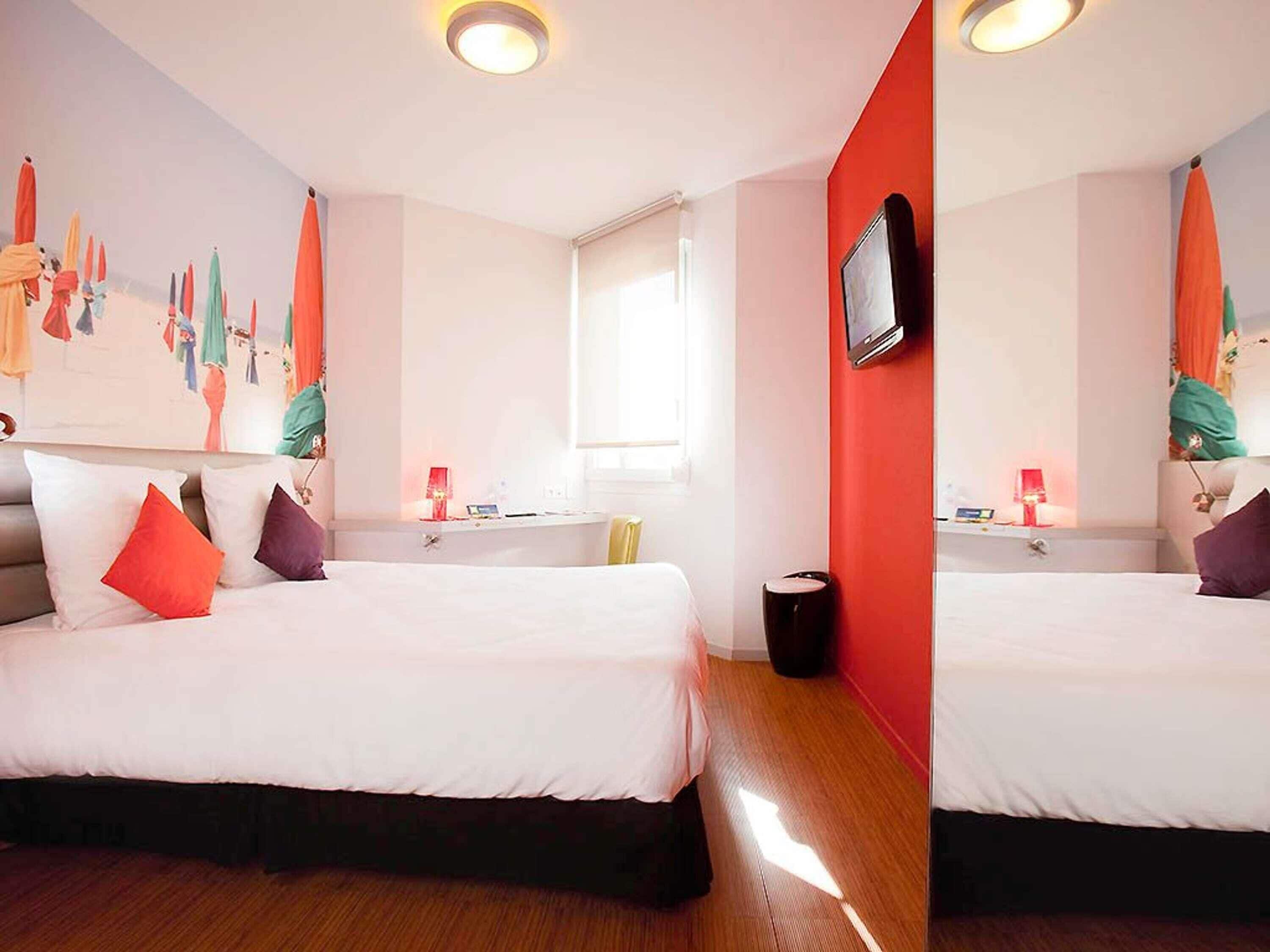 Habitació d'hotel amb un llit, una televisió, una finestra i una paret amb un mural colorit.