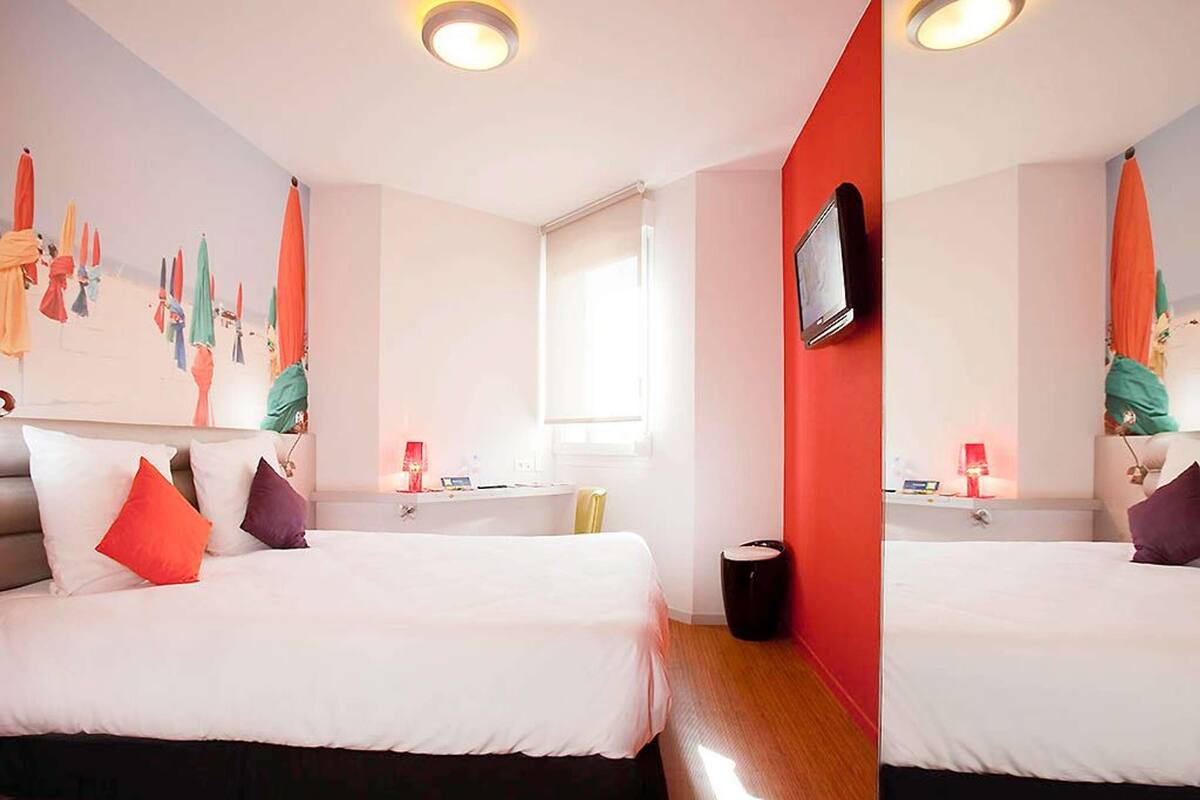 A hotel room with a bed, a television, a window, and a wall with a colorful mural.