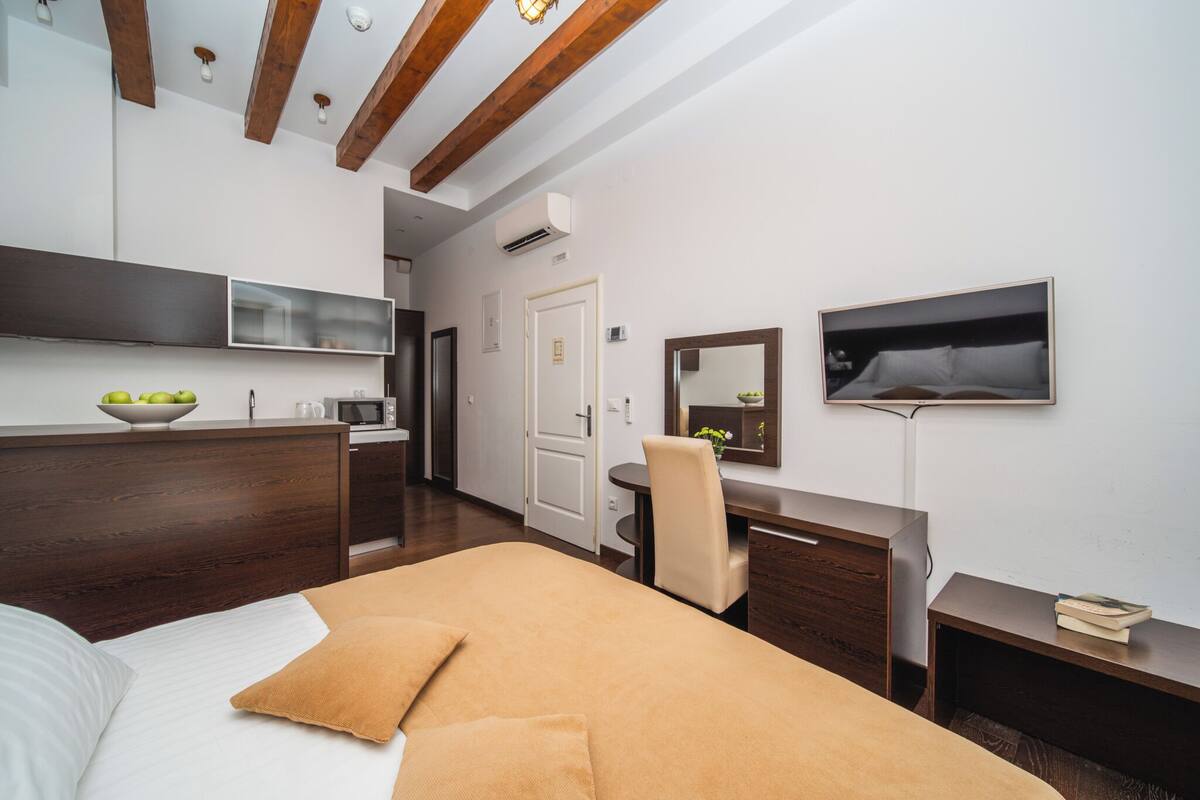 A modern hotel room with a bed, desk, chair, and a television mounted on the wall.
