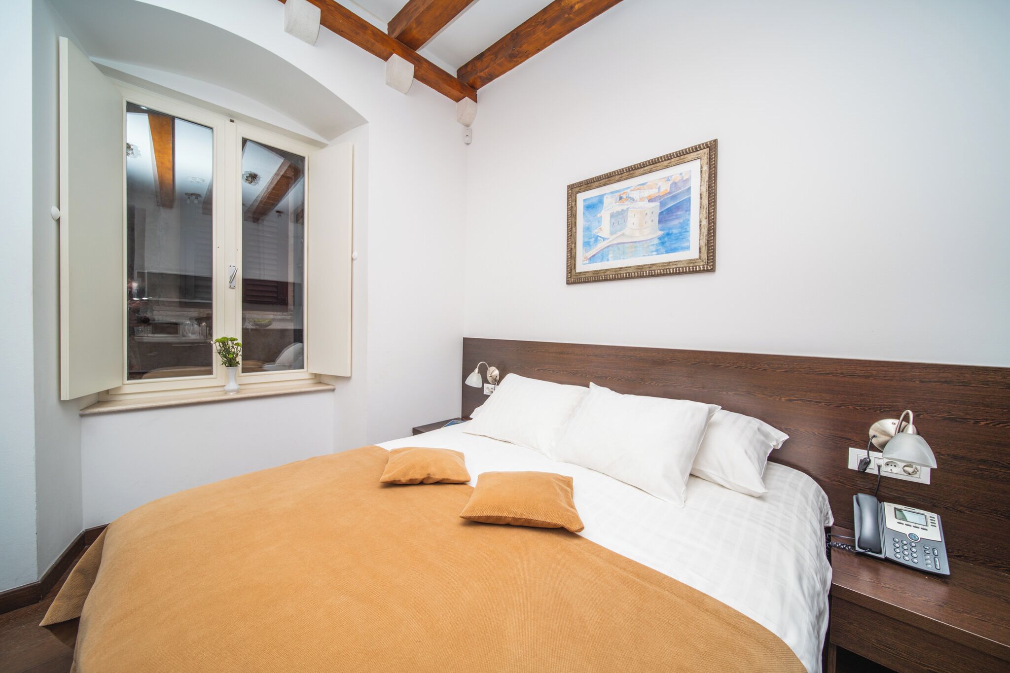A neatly made bed with white and brown bedding, a wooden headboard, and a bedside table with a lamp and phone.