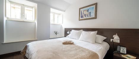 A hotel room with a large bed, a bedside table with a lamp, a phone, and a painting on the wall.