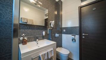 A modern bathroom with a large mirror, a white sink, a towel rack, a toilet, and a dark wooden door.