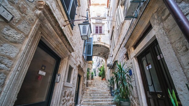 A narrow stone staircase in a historic building with multiple doors and windows, leading to an upper level. - Celenga Apartments with free offsite parking (Dubrovnik)