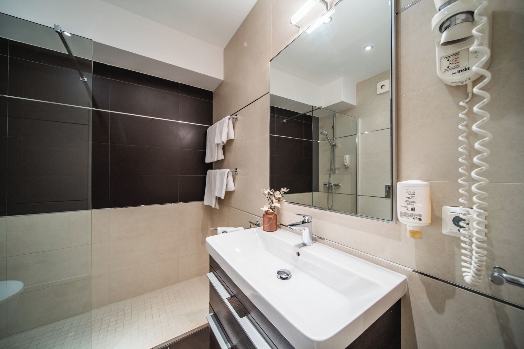 A modern bathroom with a large mirror, a white sink, and a glass shower enclosure.