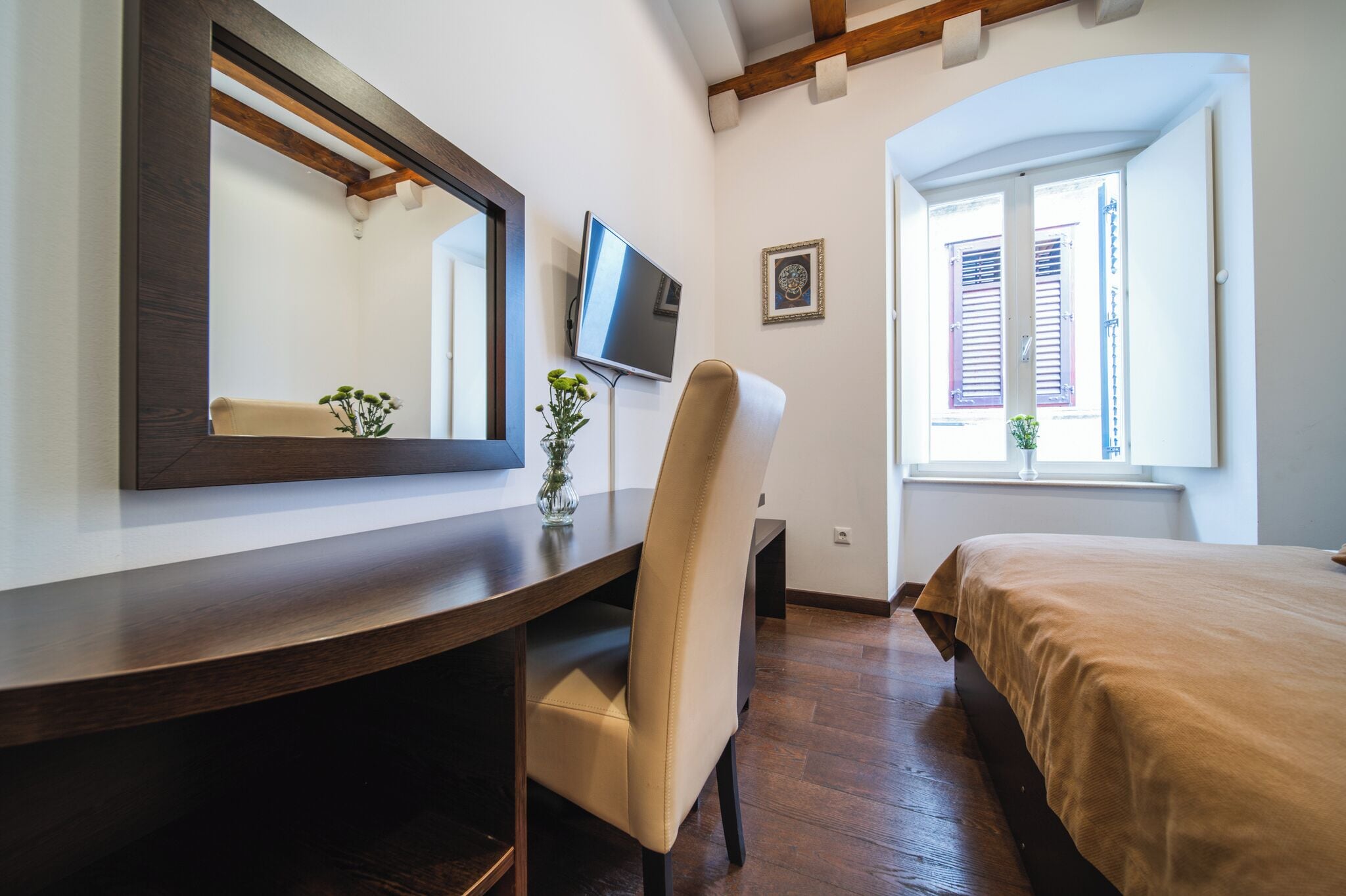 Una habitación de hotel con un escritorio de madera, una silla, una cama, un televisor y una ventana con contraventanas.