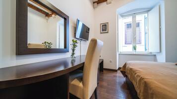 Una habitación de hotel con un escritorio de madera, una silla, una cama, un televisor y una ventana con contraventanas.