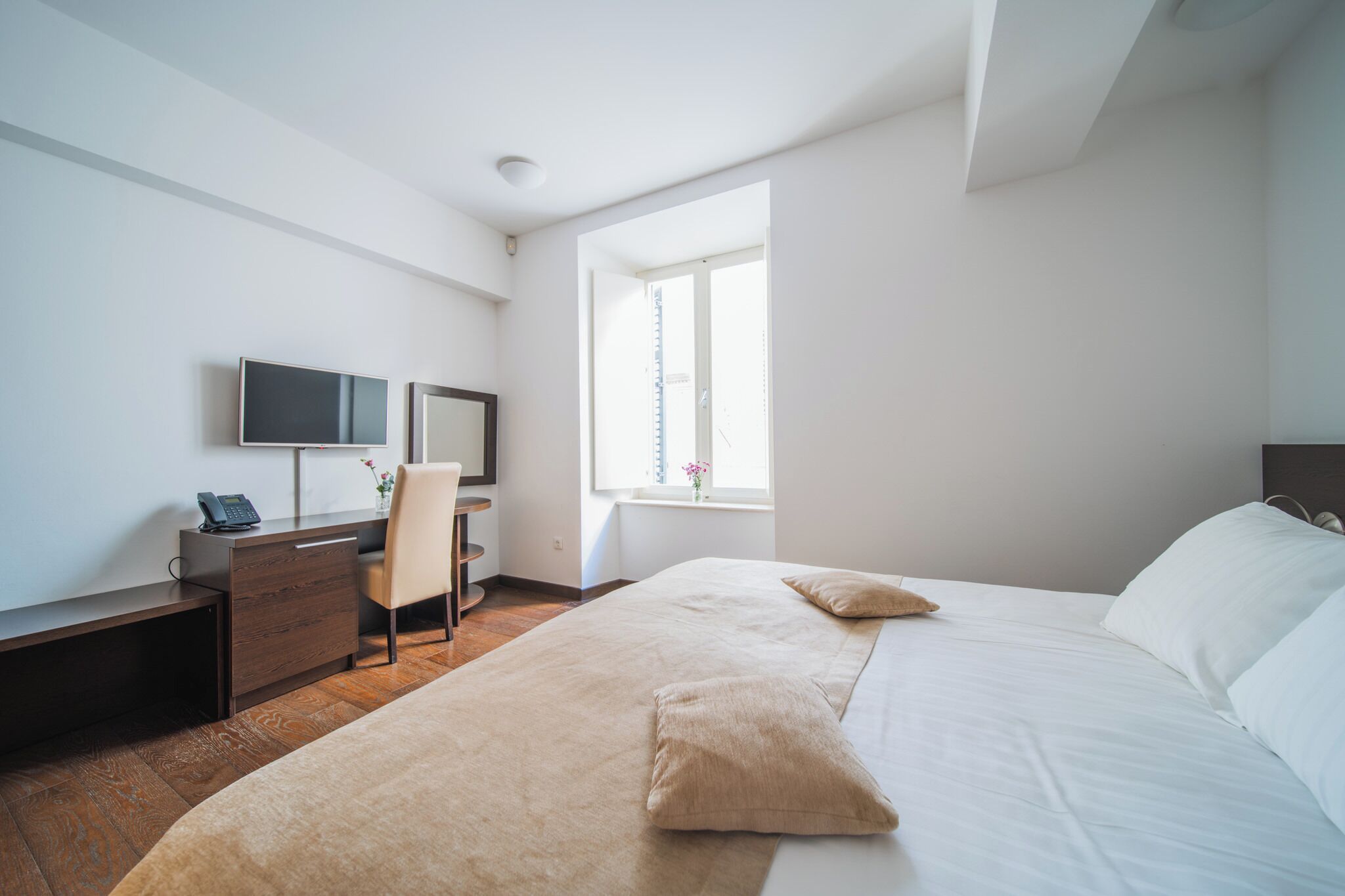 A hotel room with a bed, a desk with a chair, a television, and a window.