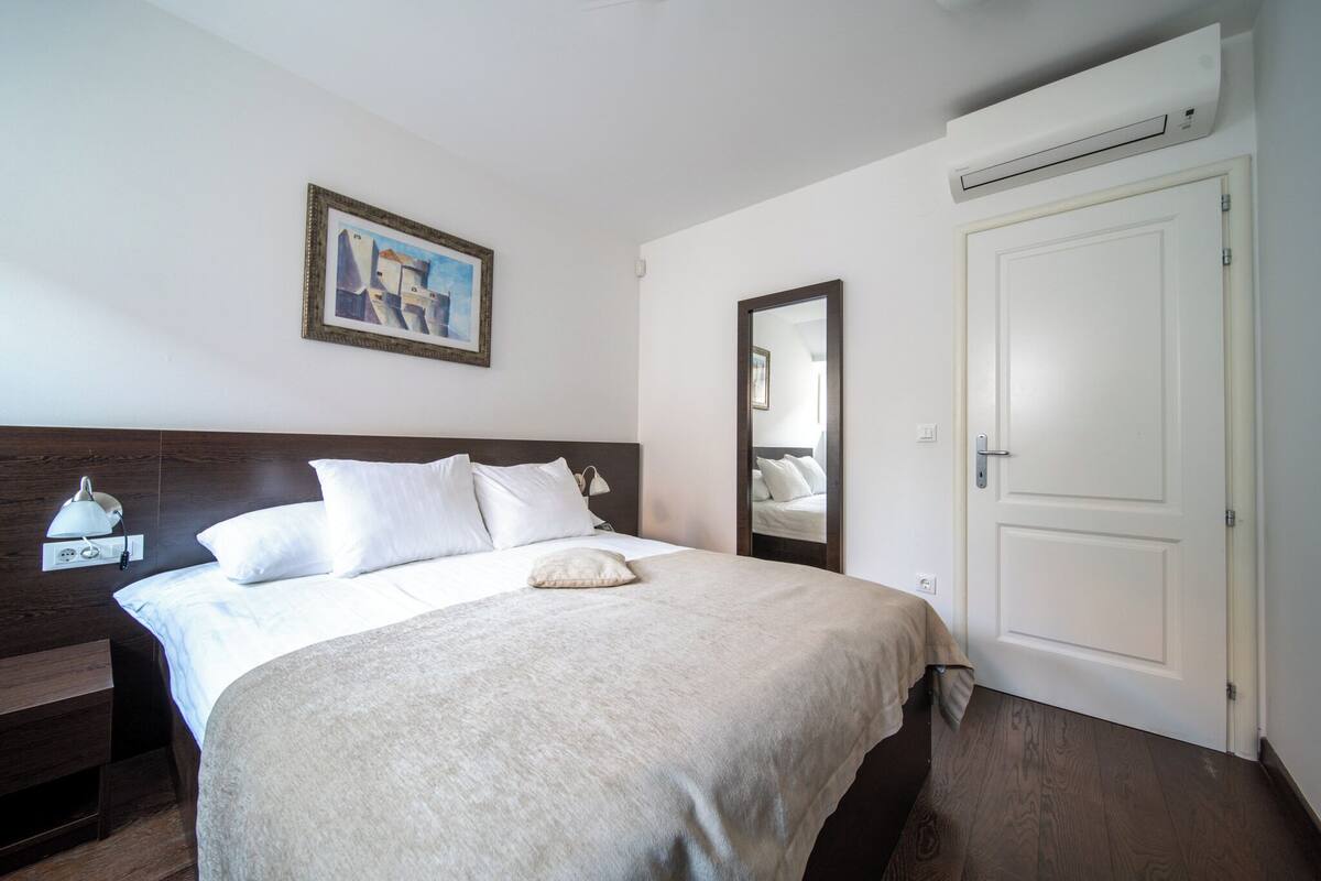 A neatly made bed with white linens and a beige throw blanket, a bedside lamp, and a framed picture on the wall.