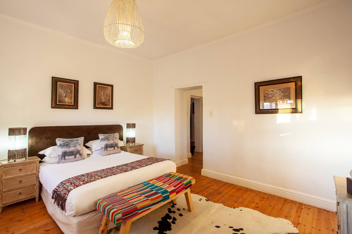 A bedroom with a large bed, wooden nightstands, a bench, and framed artwork on the walls.