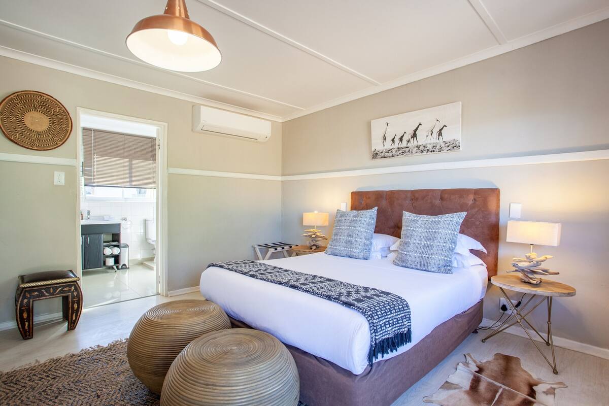 A spacious bedroom with a large bed, two bedside tables with lamps, a decorative wall hanging, and a view into the bathroom.