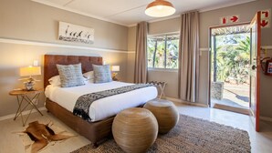 A bedroom with a large bed, a wooden headboard, a ceiling light, a nightstand, a lamp, a door with a view of the outdoors, and a rug. - Inverdoorn Private Game Reserve (Breede River)