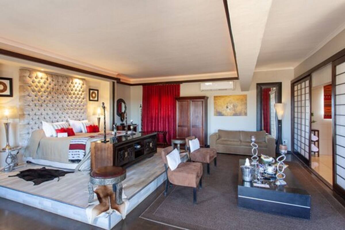 A spacious hotel room with a large bed, a sitting area with a sofa and chairs, a small dining table, and a decorative wall.