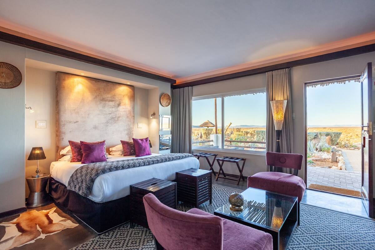 A hotel room with a large bed, a desk, a chair, and a view of the desert landscape.