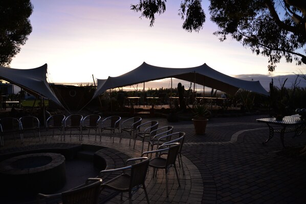 An outdoor seating area with chairs and tables under large canopies, a fire pit, and a view of the landscape. - Inverdoorn Private Game Reserve (Breede River)