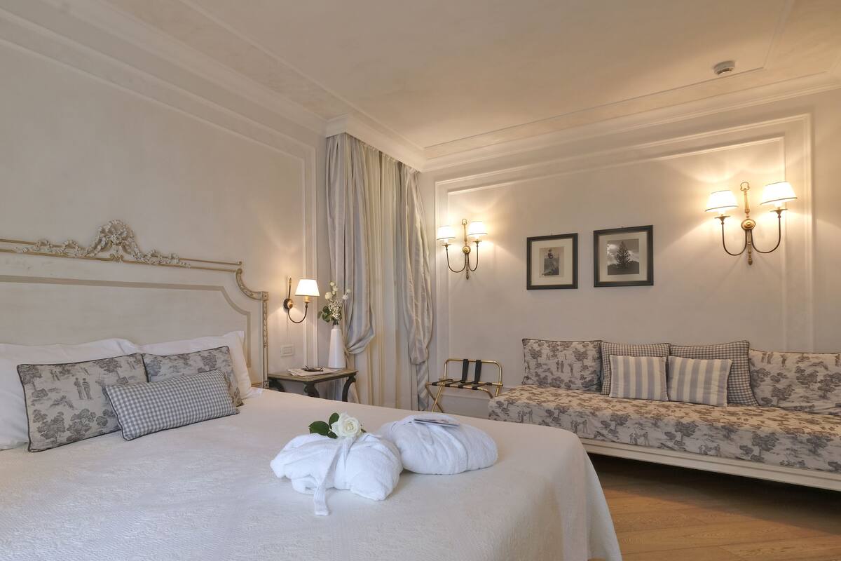 Una habitación de hotel con una cama grande, un sofá y dos lámparas fijadas a la pared.