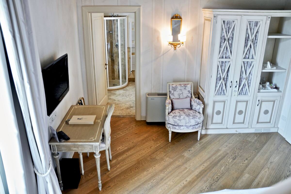 Una habitación con piso de madera, televisión, una mesita con control remoto, una silla y un armario con espejo.