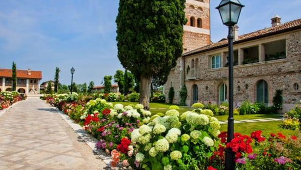 Un sendero bordeado de flores coloridas que lleva a un edificio de piedra con una torre.