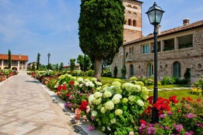 A pathway lined with vibrant flowers leading to a stone building with a tower. - Garda Hotel San Vigilio Golf (Pozzolengo)