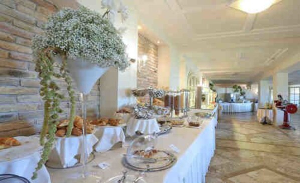 A buffet setup with various food items on tables, a brick wall, and a hanging floral arrangement.