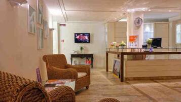 Una hall con scrivania della reception, mobili in vimini, televisore e opere d'arte incorniciate alle pareti.