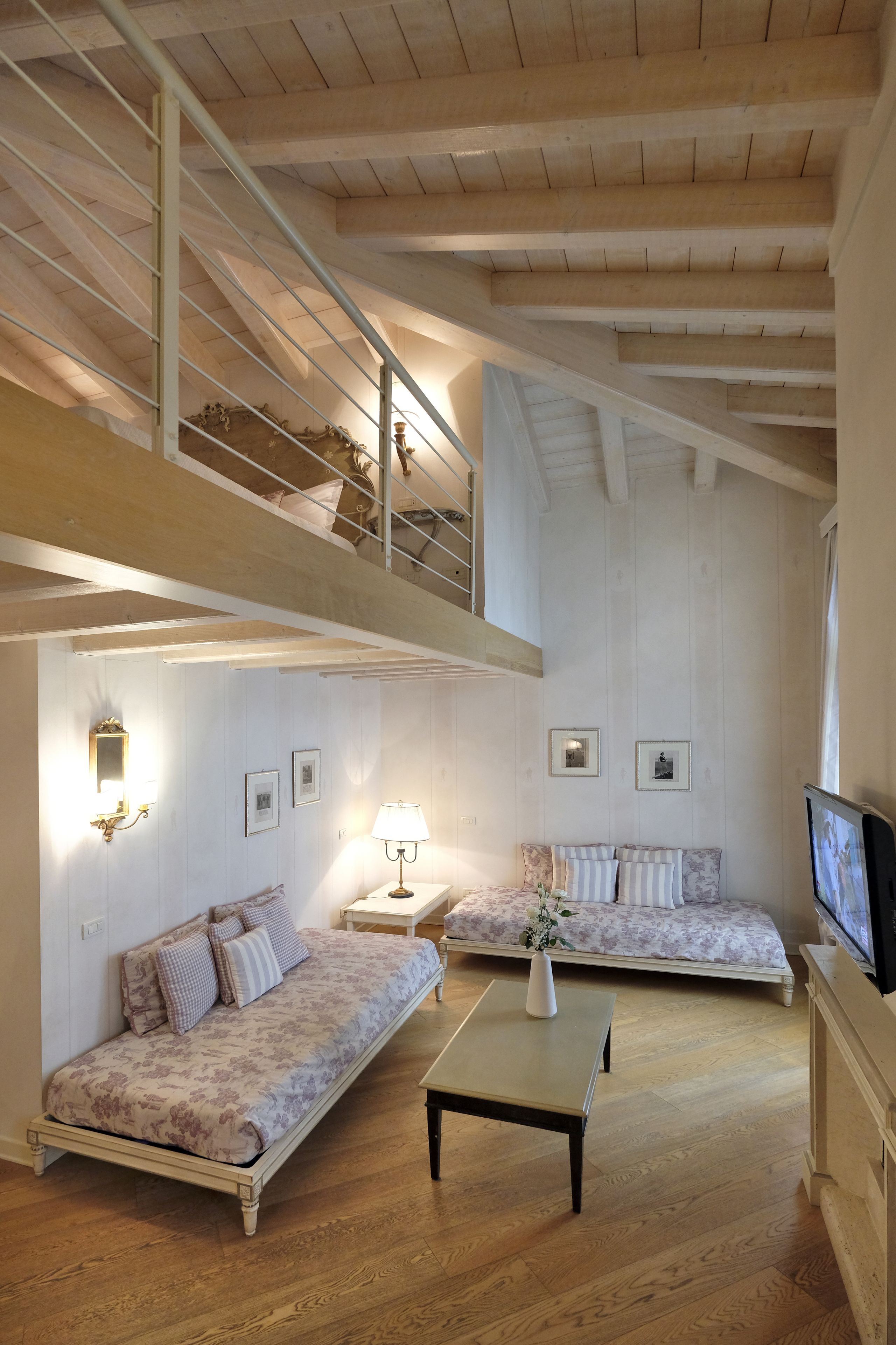 Een ruime loft-achtige kamer met een hoge plafond, houten balken, een inbouwtrappenhuis, twee banken, een salontafel en een televisie.