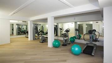 A spacious gym with various exercise equipment, including treadmills and weight machines, and large mirrors on the walls.