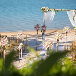 Romantic beach wedding setup with a floral arch and rows of chairs.