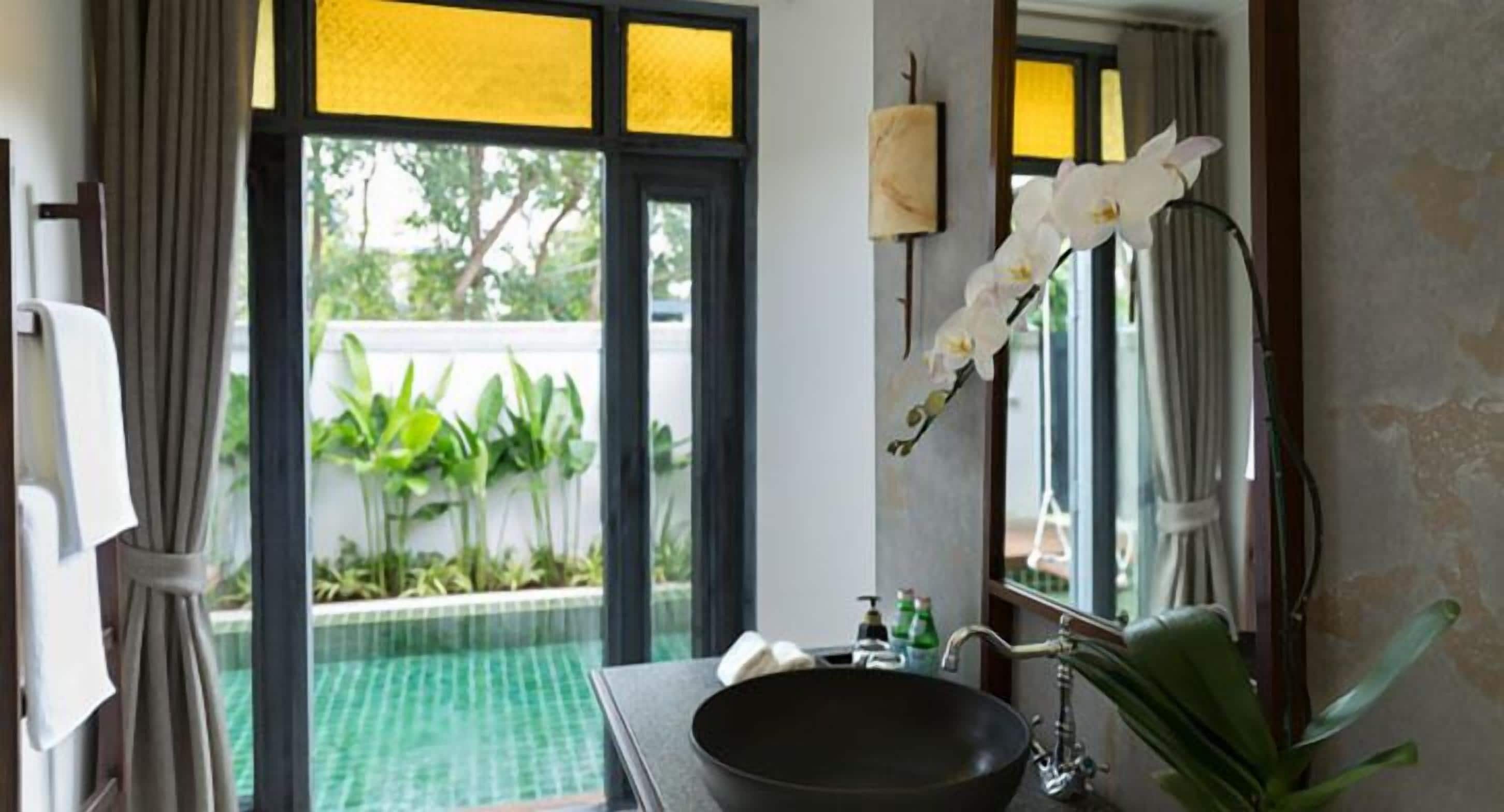Une salle de bain dotée d’un grand lavabo, d’un miroir et donnant sur une piscine extérieure.