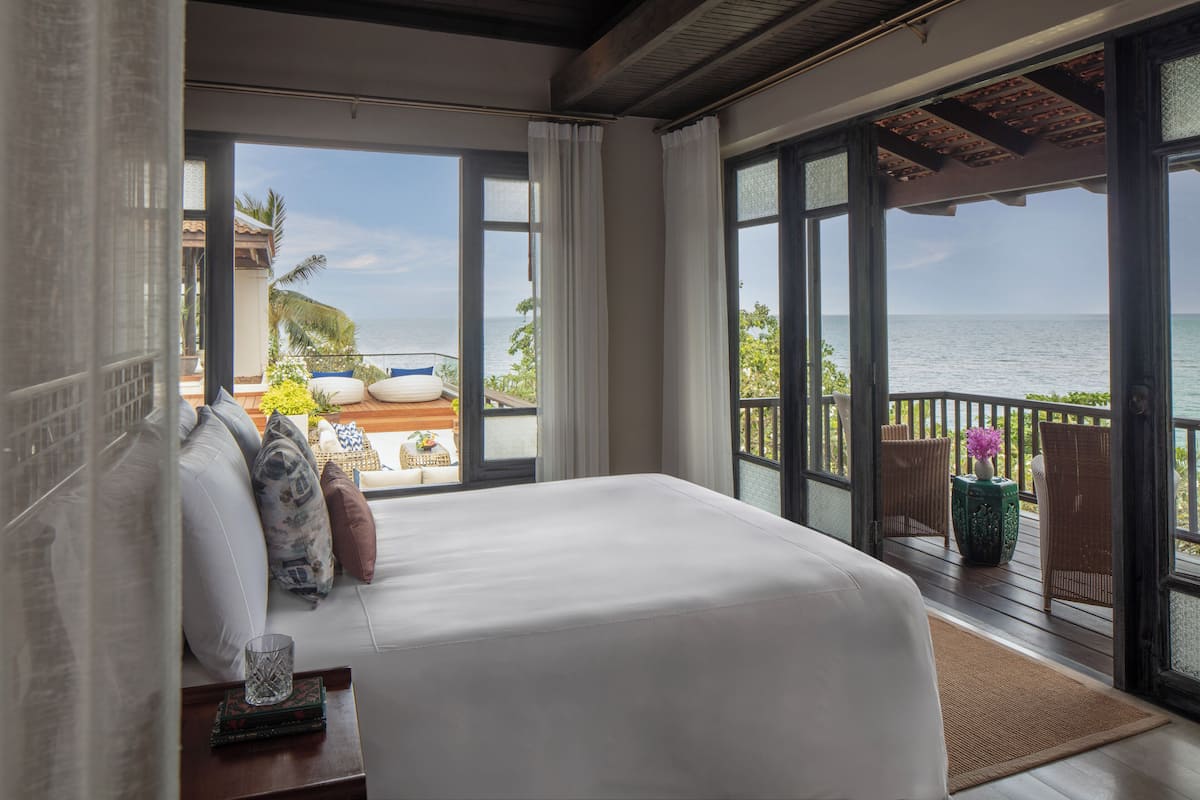 A bedroom with a large bed, a view of the ocean, and a balcony with wicker furniture.