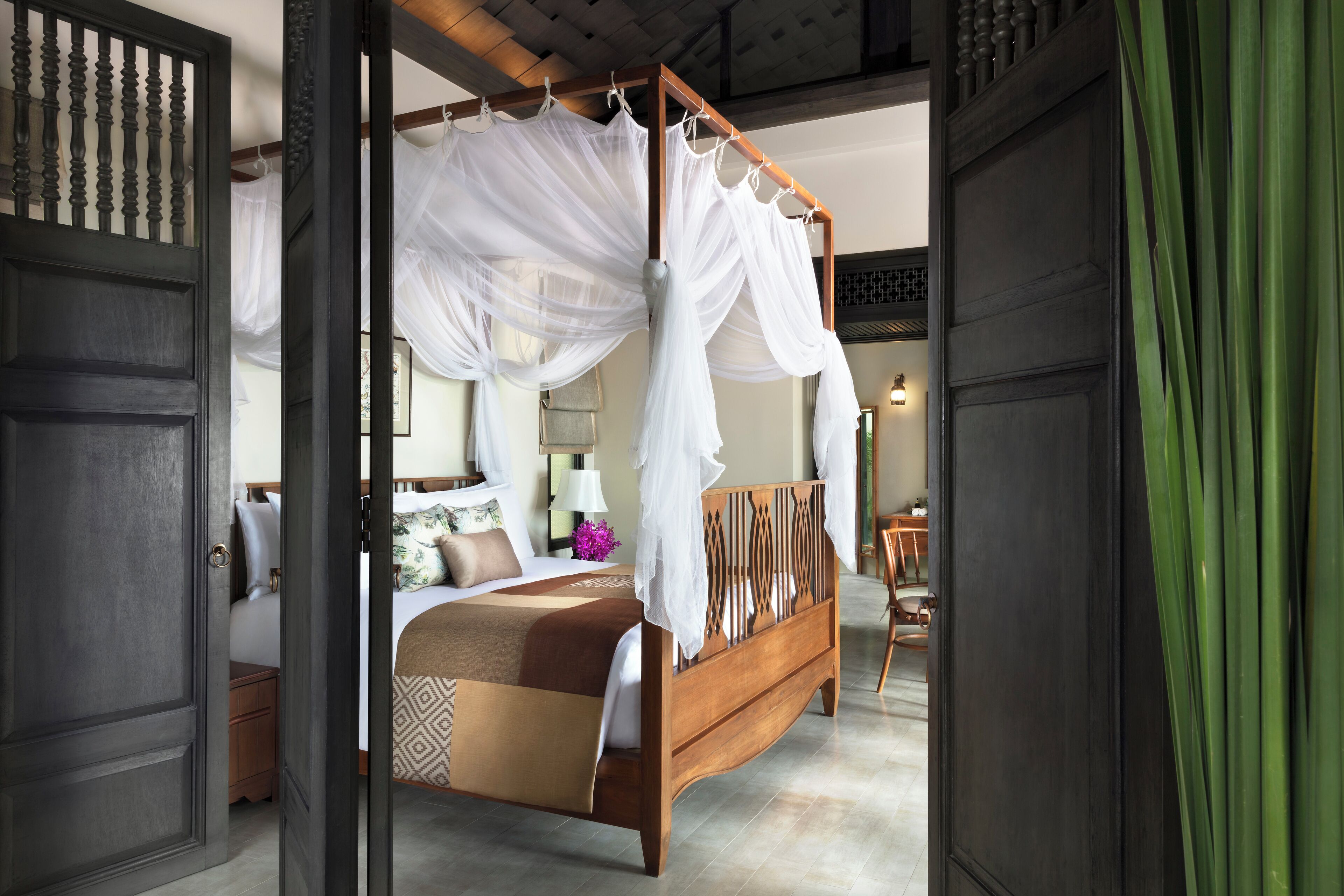 A four-poster bed with white drapes, a wooden headboard, and a patterned bedspread.