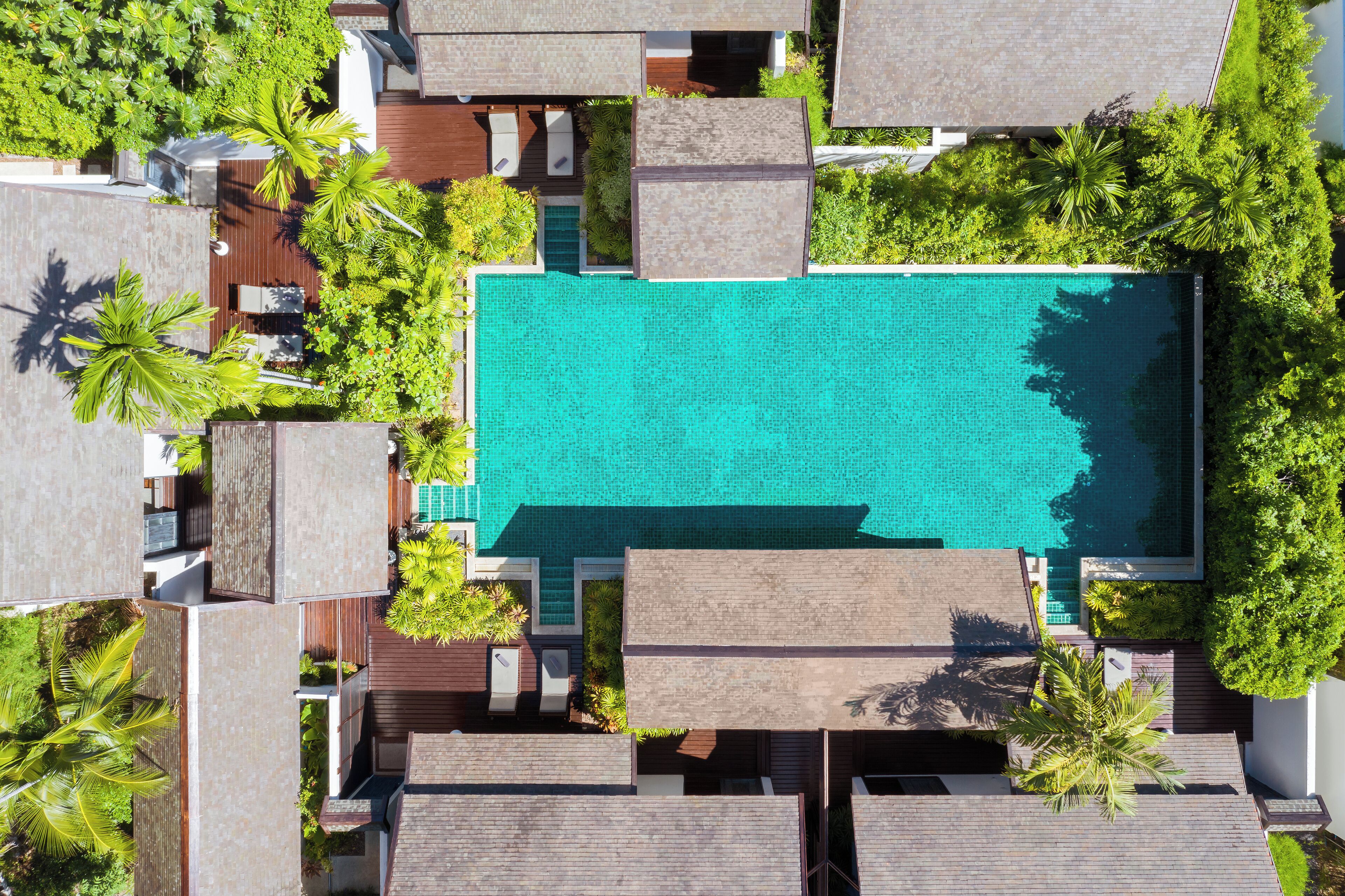 Vista aérea de un complejo turístico con una piscina central rodeada de exuberante vegetación y edificios modernos.