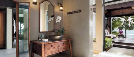 A modern bathroom with a large mirror, wooden vanity, and a view of the ocean.