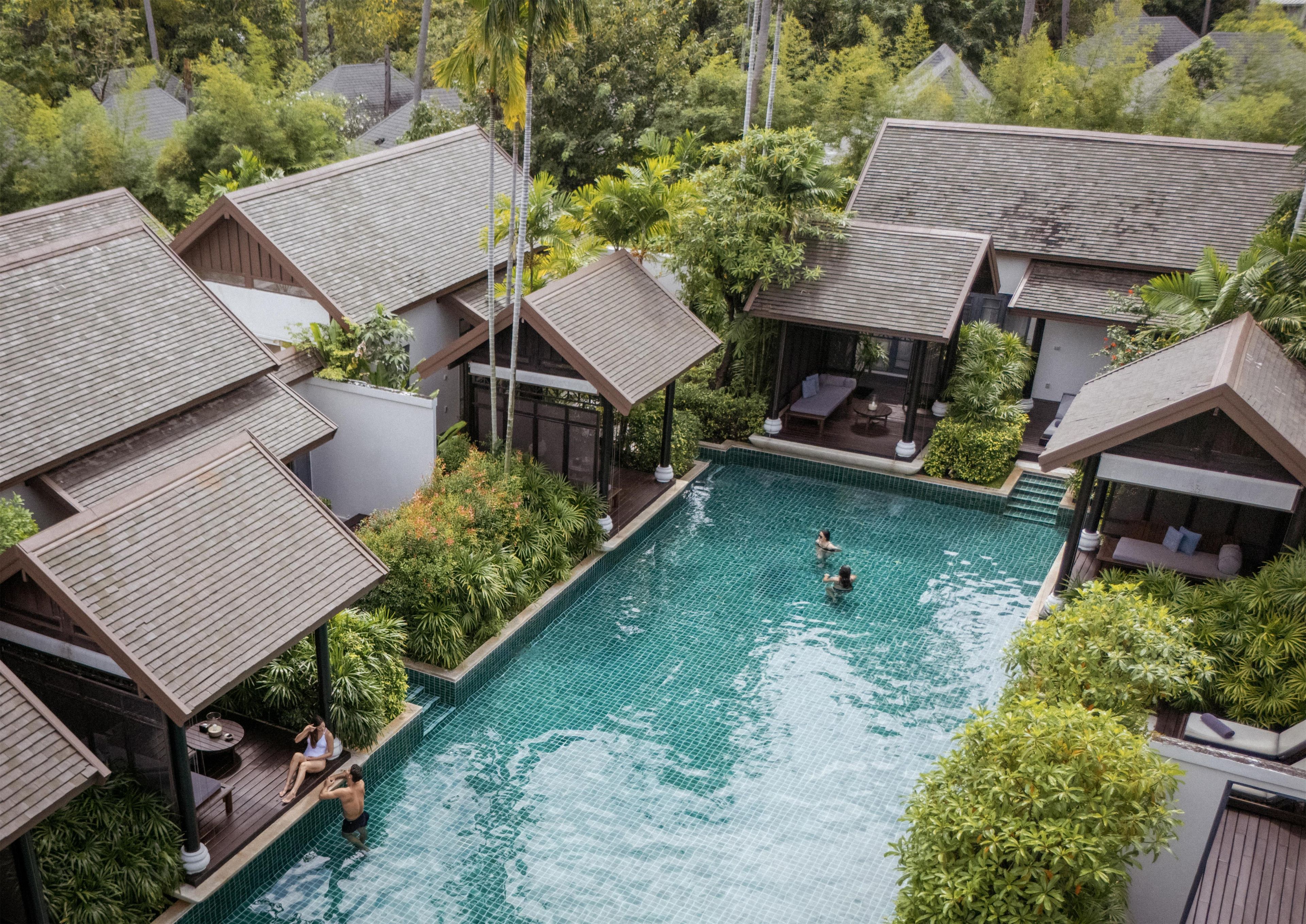 A resort with multiple overwater bungalows, a central swimming pool, and lush greenery.