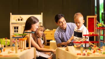 A family interacting with a wooden playhouse and various toys in a room with a simple layout and neutral decor.