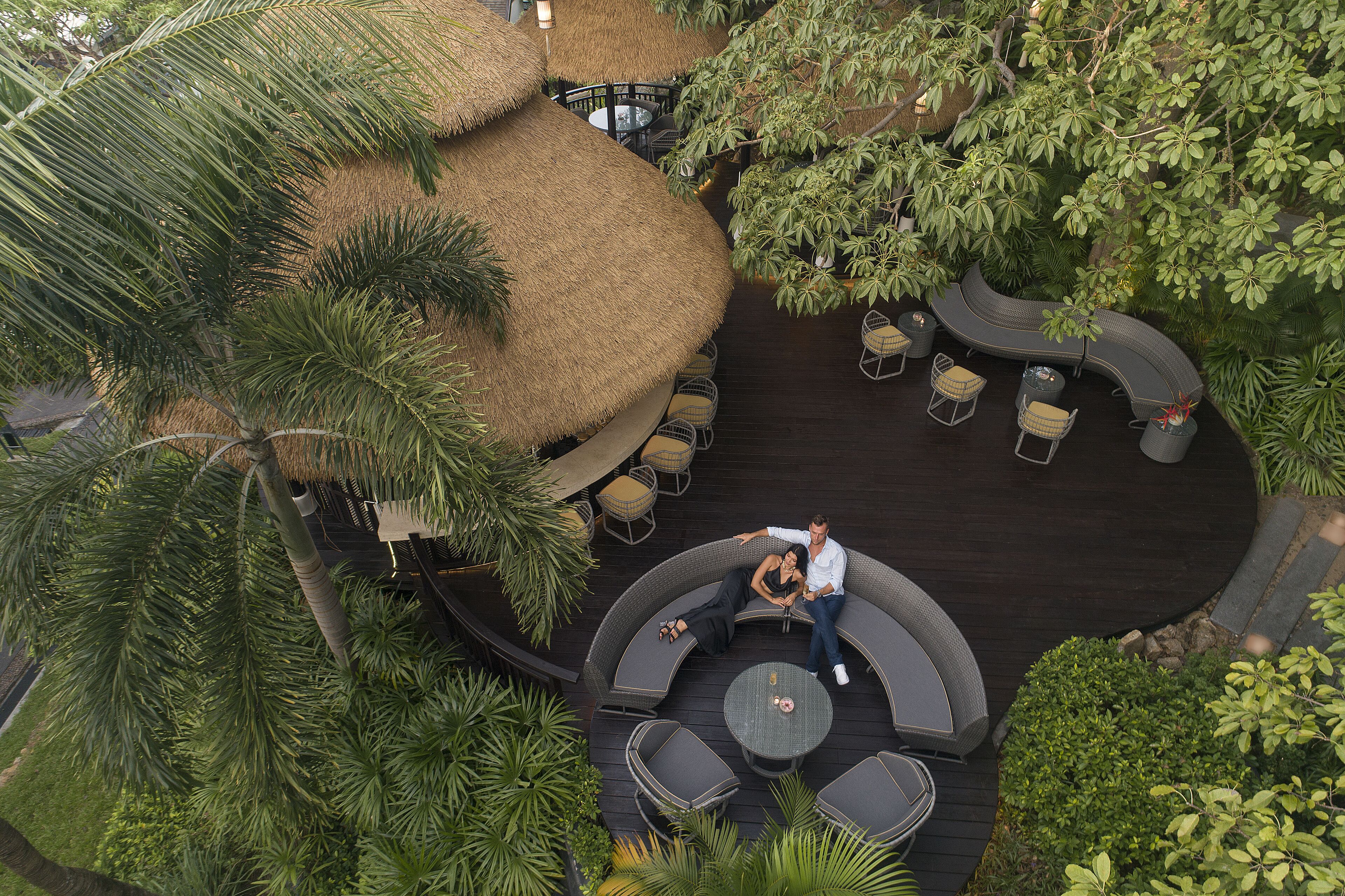 An outdoor seating area with round tables and chairs, surrounded by lush greenery and palm trees.