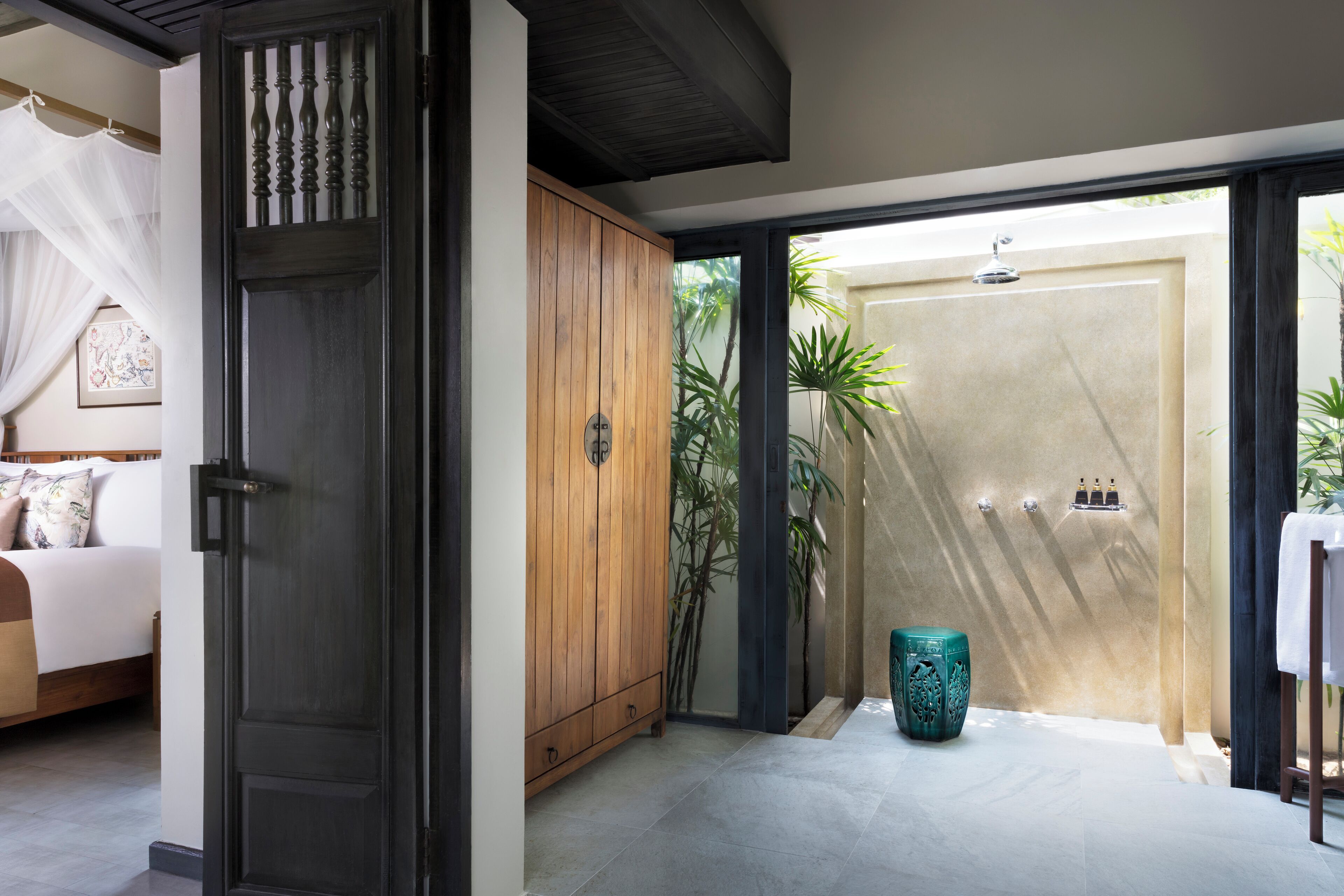 Una habitación con una cama, un armario de madera, un taburete decorativo verde y una zona de ducha con puerta de cristal.