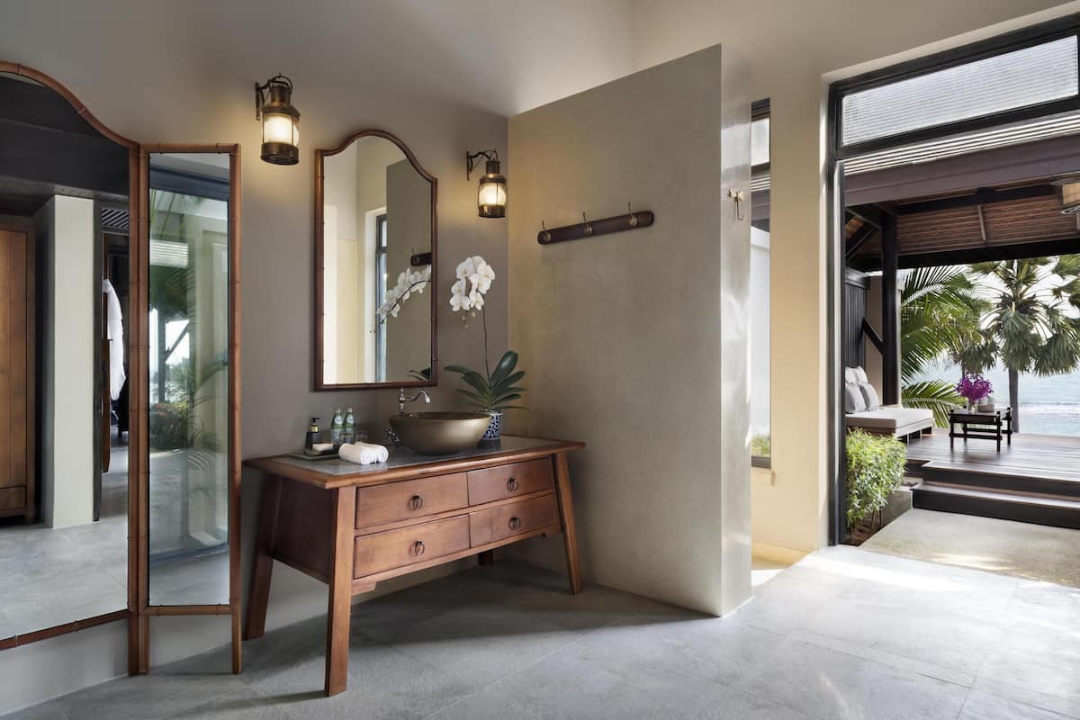 A bathroom with a wooden vanity, a large mirror, and a view of the ocean.