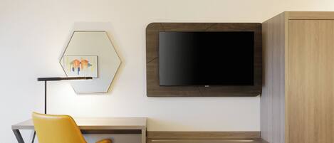 Ein Hotelzimmer mit einem Bett, einem Schreibtisch mit Stuhl, einem an der Wand befestigten Fernseher und einem Kleiderschrank.