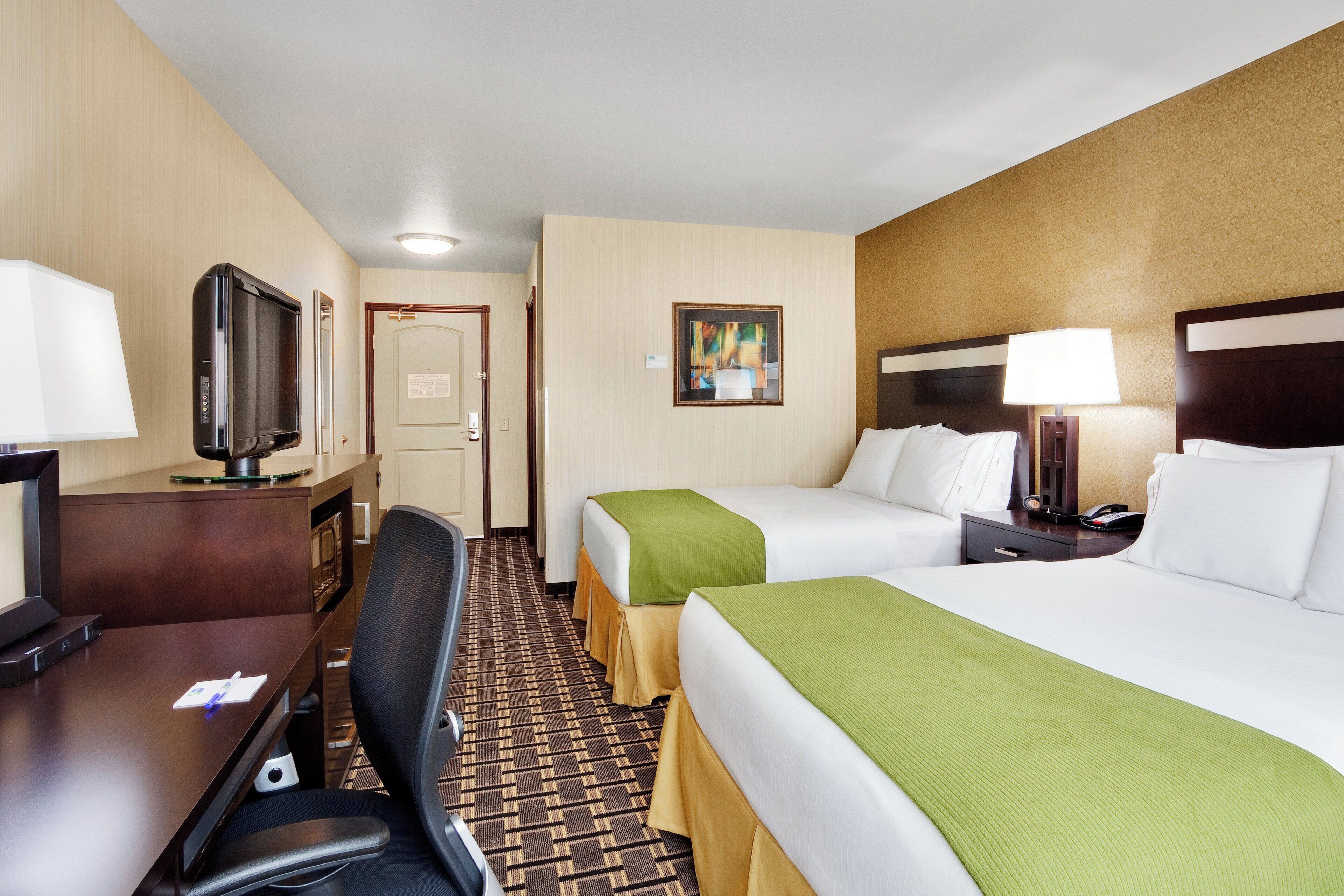 A hotel room with two beds, a desk with a television, a chair, and a carpeted floor.