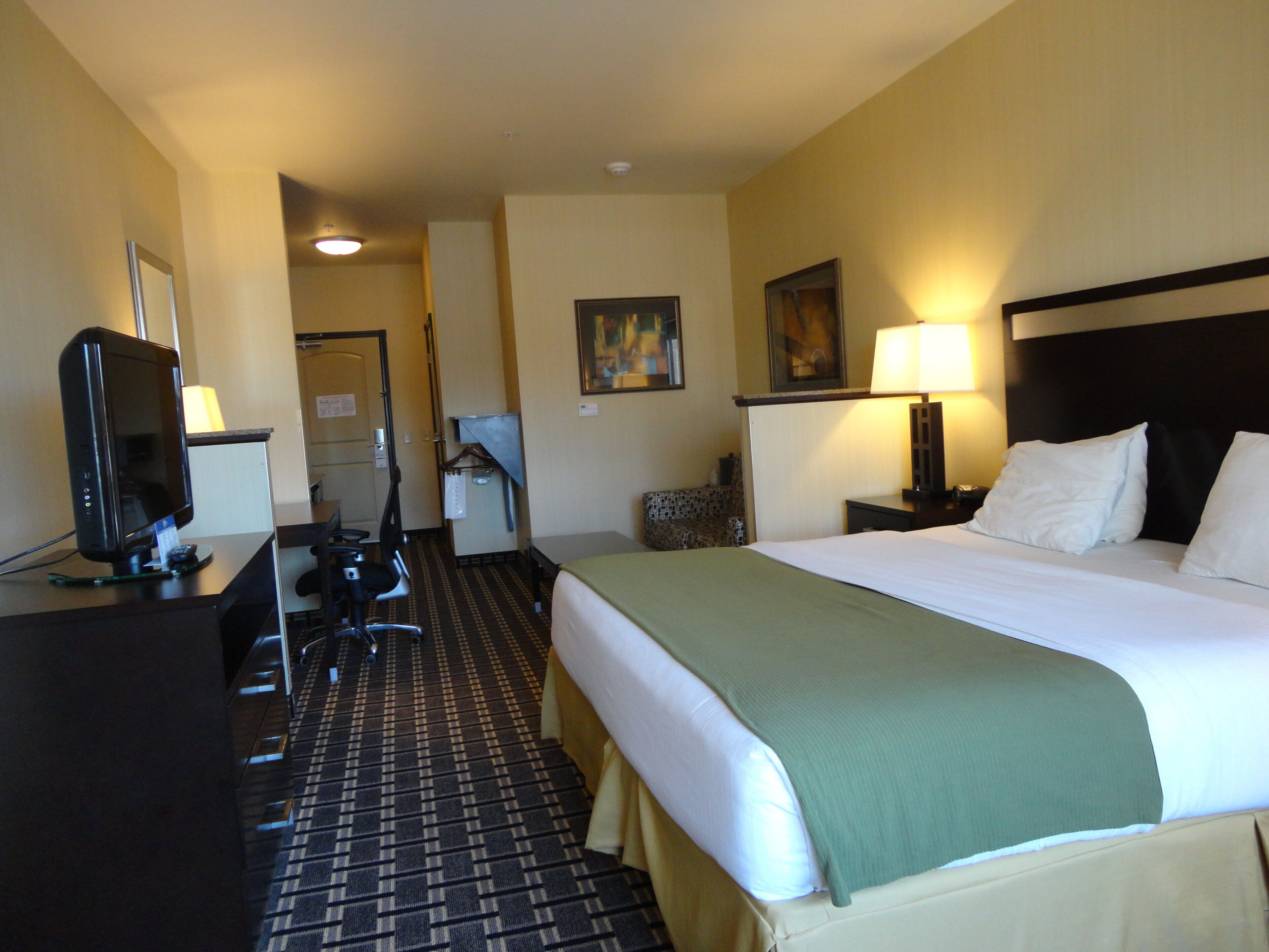 Une chambre d’hôtel avec un lit, un bureau équipé d’un ordinateur, une chaise, une lampe et un tableau au mur.