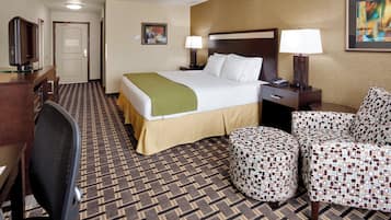 A hotel room with a bed, a desk, a chair, a lamp, and a painting on the wall.
