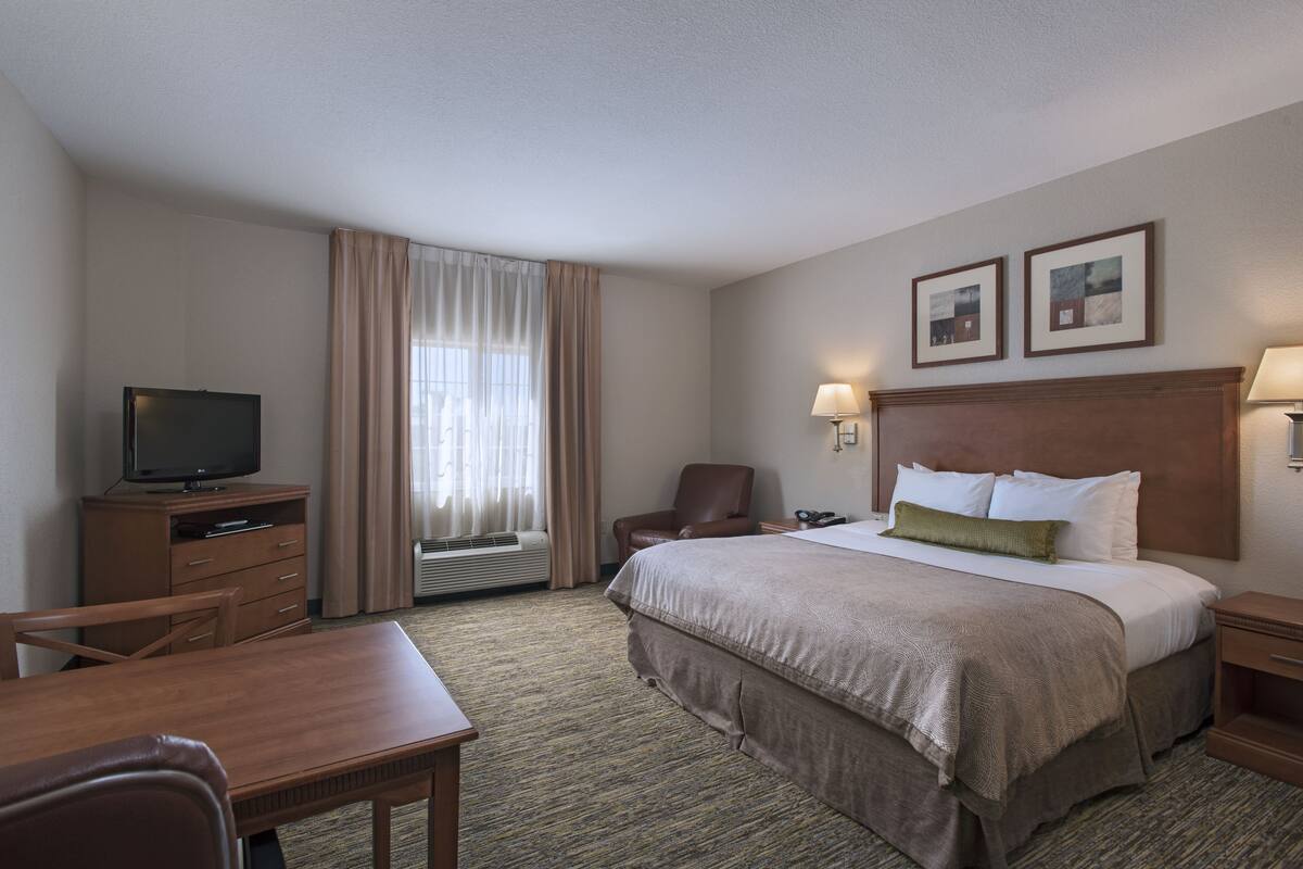 Een hotelkamer met een bed, een bureau, een stoel, een televisietoestel en een raam met gordijnen.