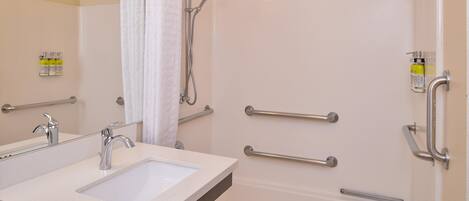 A bathroom with a sink, mirror, shower, and grab bars.