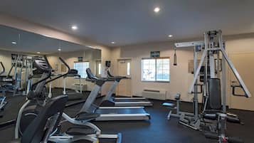 Un gimnasio con cintas de correr, máquinas de pesas y un espejo.