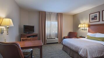 A hotel room with a bed, a desk, a chair, a television, a lamp, and a window with curtains.
