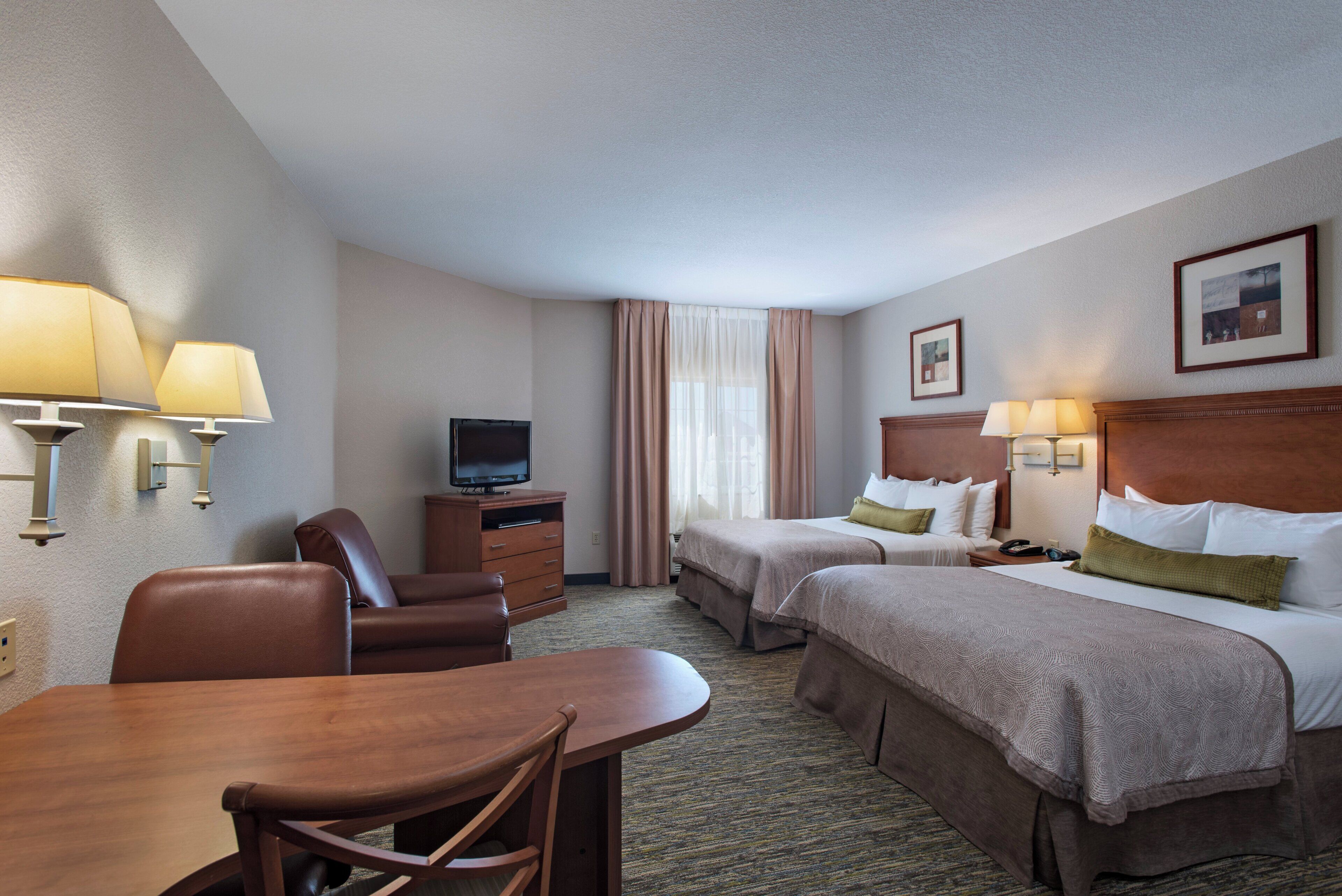 A hotel room with two beds, a desk, a chair, a television, and a lamp.