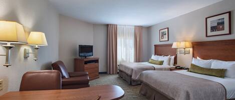 A hotel room with two beds, a desk, a chair, a television, and a lamp.